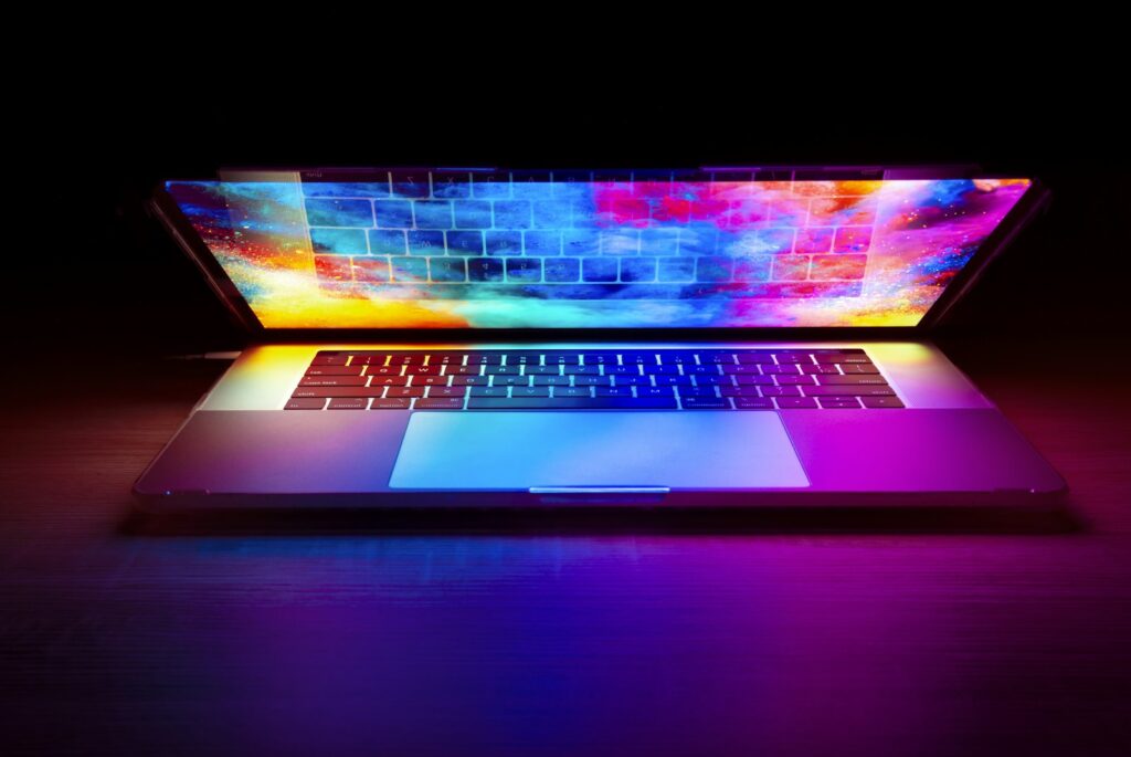 Laptop with a vibrant, colourful screen glowing on a dark wooden desk