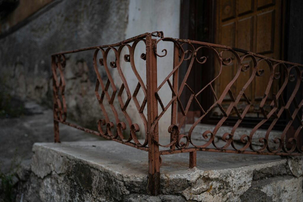 A rusted wrought iron railing on a stone porch in front of a door