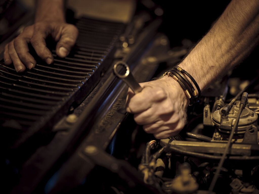 Hands with grease working on a car engine with a metal wrench during a repair