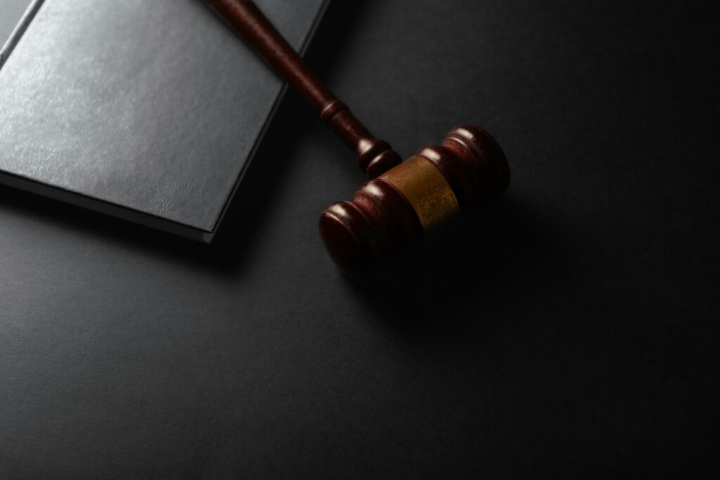Wooden judge's gavel resting on a dark surface next to a law book