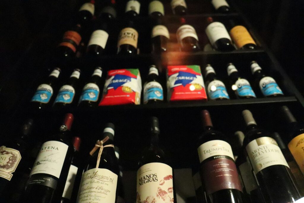 Rows of wine and beer bottles stored on dark wooden shelves in a dimly lit room