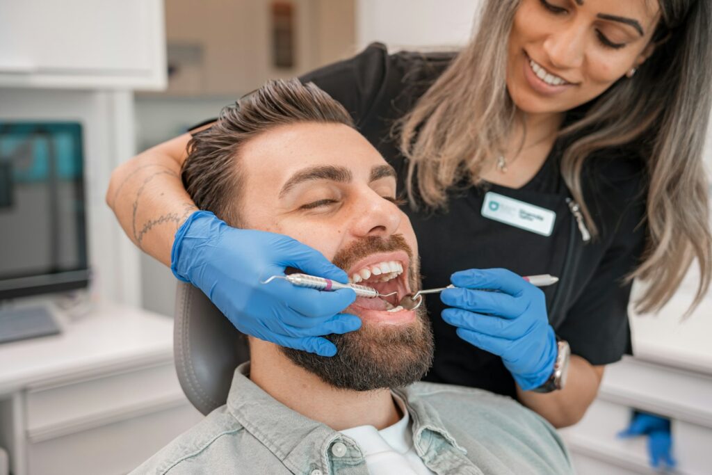 Dentist in blue gloves examining a man's teeth in a dental office, relevant to treatment choices